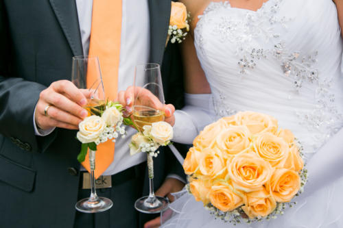hands of bride and groom holding wedding bouquet and glasses